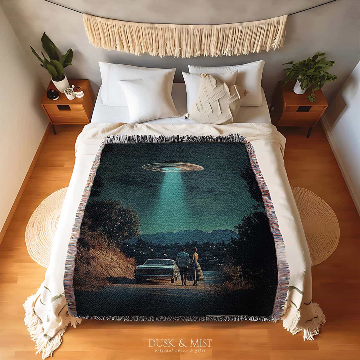 Woven cotton blanket featuring a UFO beaming light onto a couple standing near a car at night, with a starry sky and silhouetted trees.
