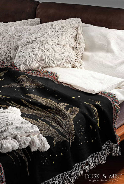 Woven cotton blanket with golden occult illustrations — palmistry hand, crescent moon, moth, snake, crystals, plants, and celestial symbols on a black background.