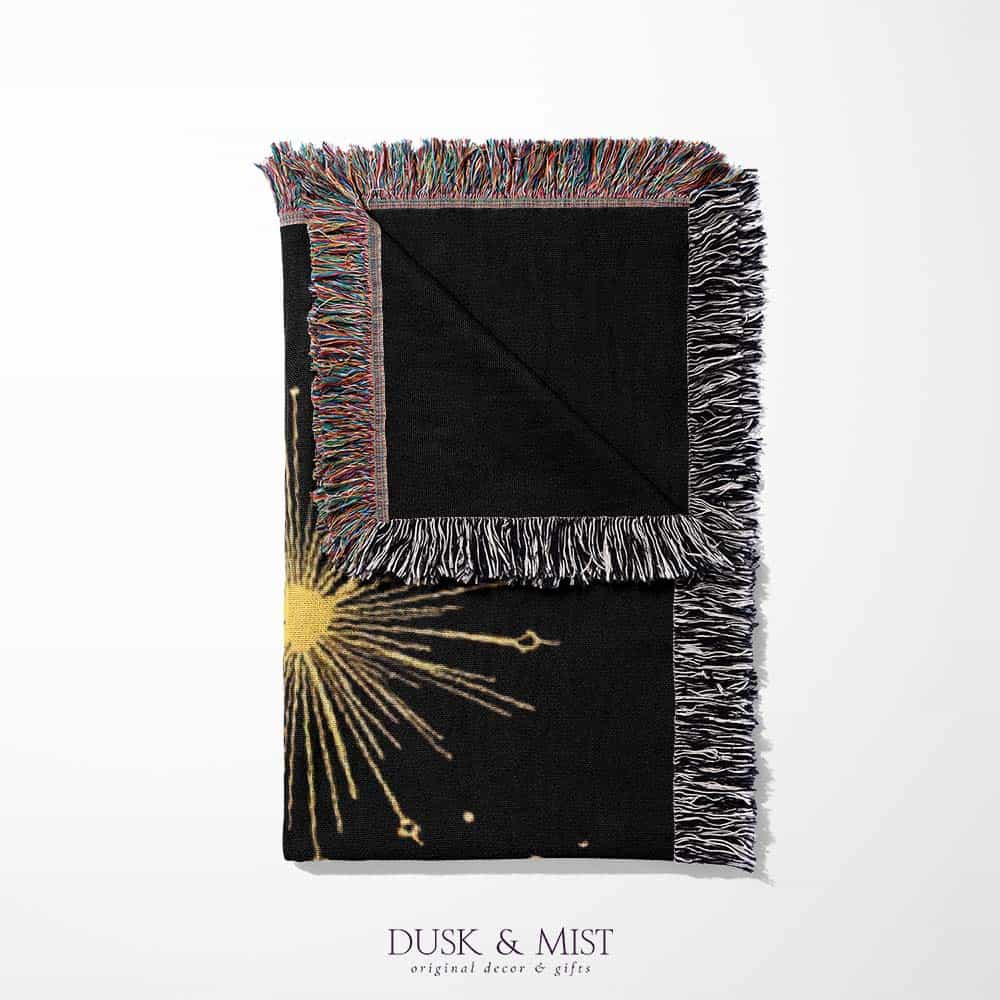 Woven cotton blanket with golden occult illustrations — palmistry hand, crescent moon, moth, snake, crystals, plants, and celestial symbols on a black background.