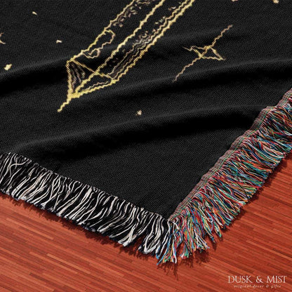 Woven cotton blanket with golden occult illustrations — palmistry hand, crescent moon, moth, snake, crystals, plants, and celestial symbols on a black background.