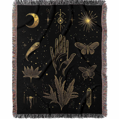 Woven cotton blanket with golden occult illustrations — palmistry hand, crescent moon, moth, snake, crystals, plants, and celestial symbols on a black background.