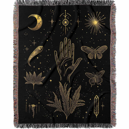Woven cotton blanket with golden occult illustrations — palmistry hand, crescent moon, moth, snake, crystals, plants, and celestial symbols on a black background.