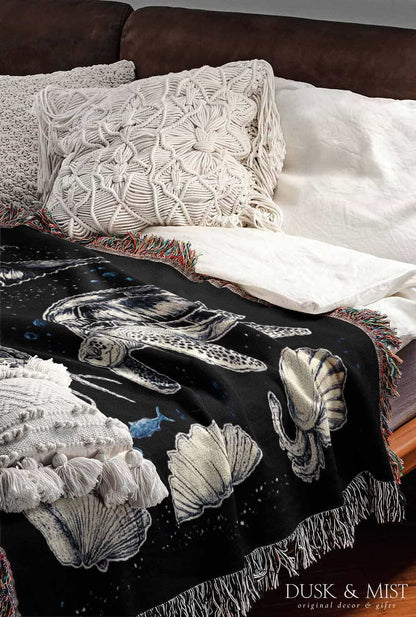 Woven cotton blanket featuring detailed marine life illustration — orca, dolphins, sea turtle, octopus, jellyfish, seashells, and fish on a black background.