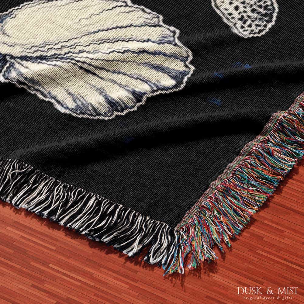 Woven cotton blanket featuring detailed marine life illustration — orca, dolphins, sea turtle, octopus, jellyfish, seashells, and fish on a black background.