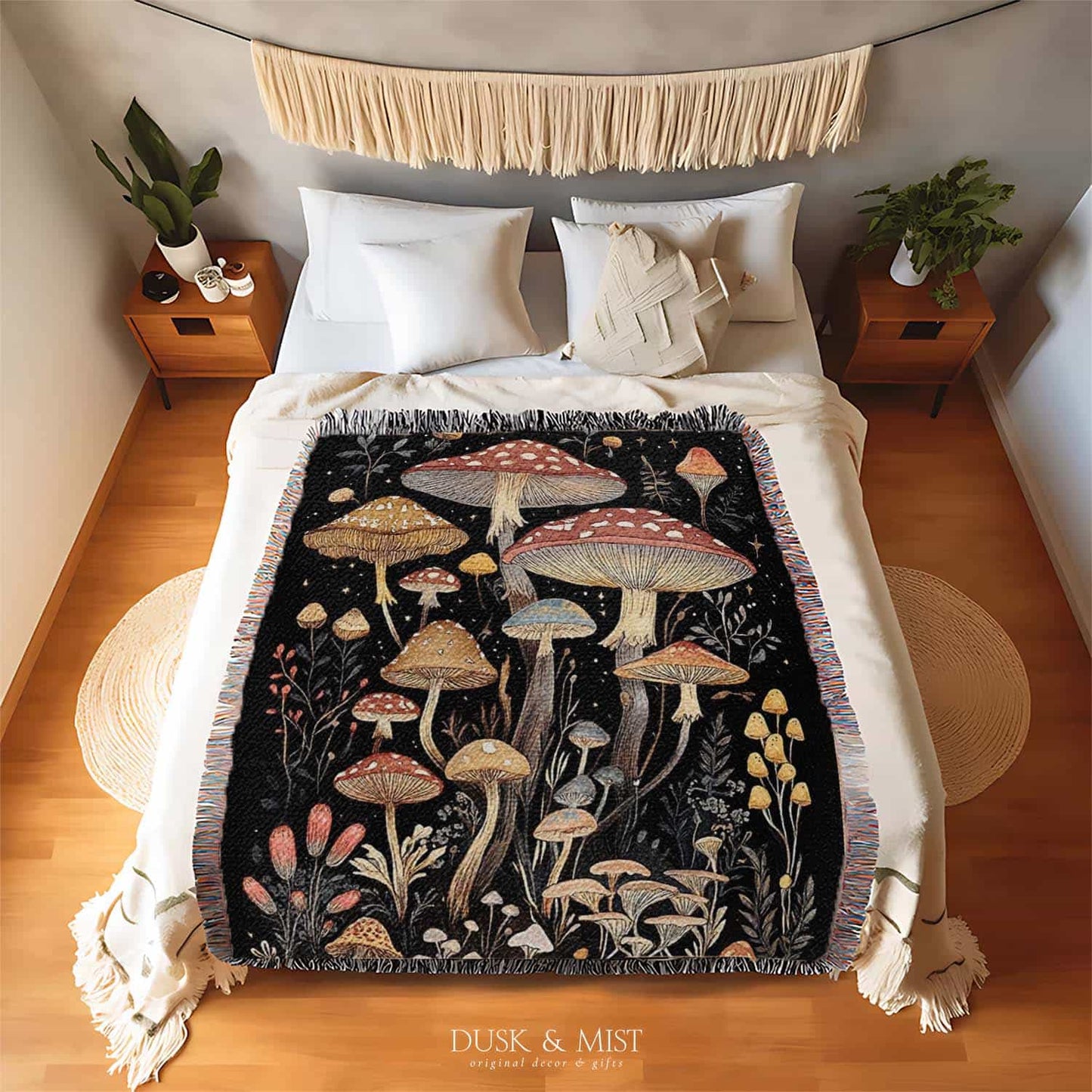 Woven cotton blanket showing a colorful cluster of mushrooms in red, gold, blue, and cream caps with surrounding plants and flowers on a black background.