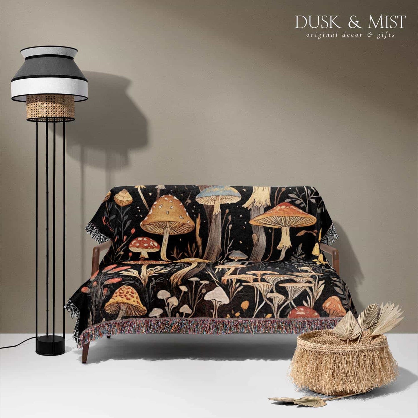 Woven cotton blanket showing a colorful cluster of mushrooms in red, gold, blue, and cream caps with surrounding plants and flowers on a black background.