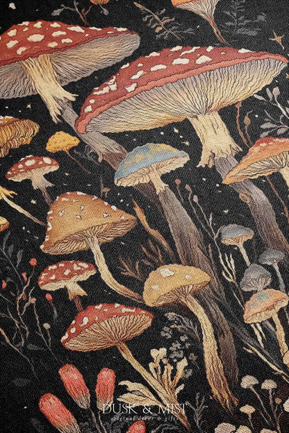 Woven cotton blanket showing a colorful cluster of mushrooms in red, gold, blue, and cream caps with surrounding plants and flowers on a black background.