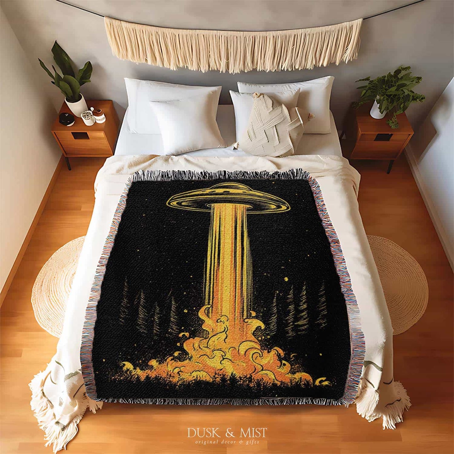 Woven cotton blanket featuring a UFO casting a golden beam into the forest at night, with glowing clouds and cosmic light effects.
