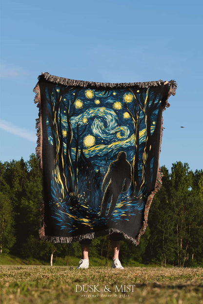 Woven cotton blanket featuring Sasquatch walking through a forest under a Van Gogh-style starry night sky with swirling stars and moonlight.