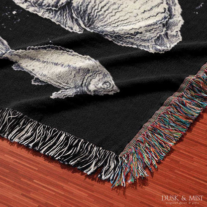 Woven cotton blanket featuring detailed ocean life illustration — whales, orca, turtles, jellyfish, octopus, seashells, fish, and coral on a black background.