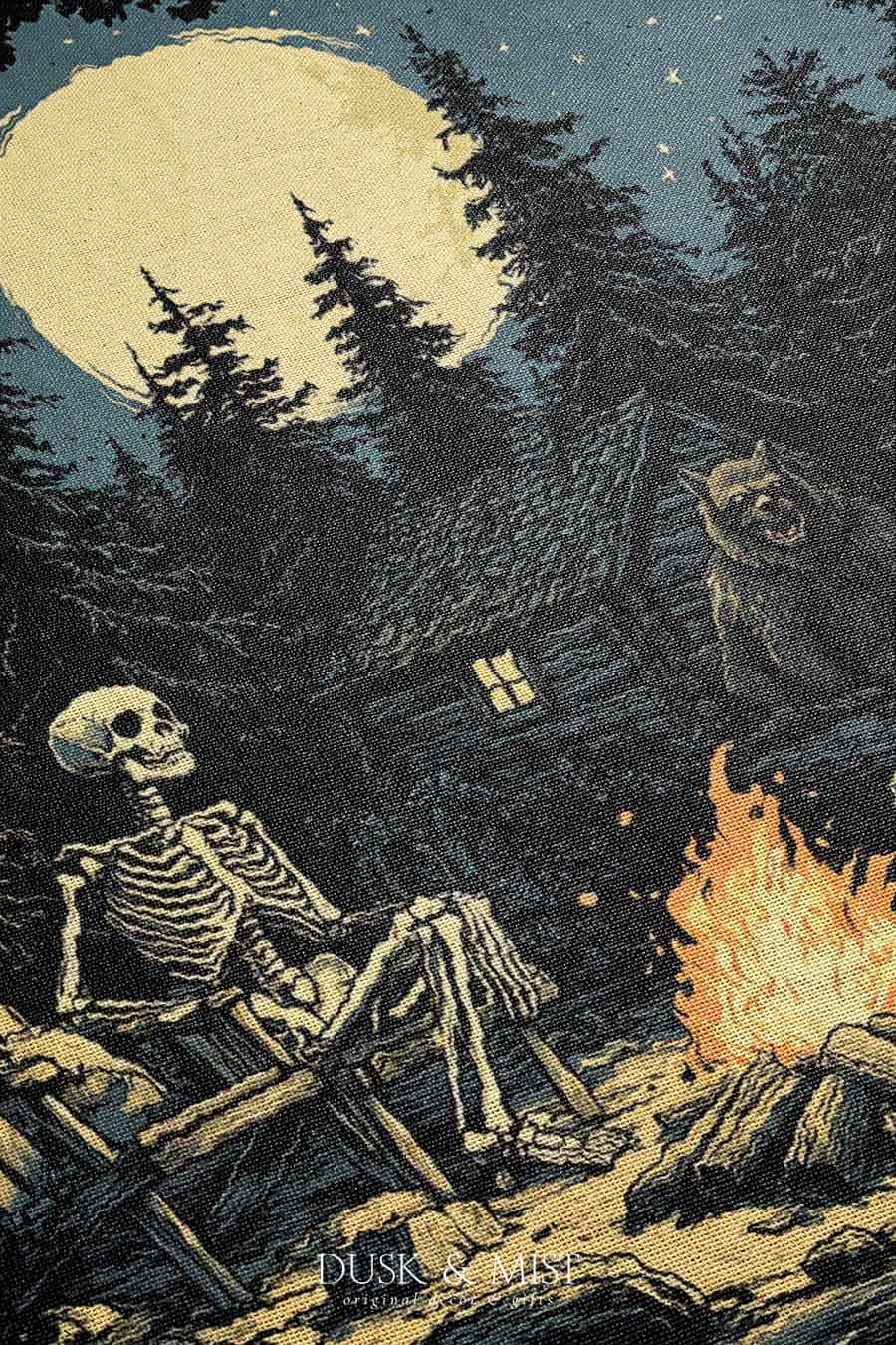 Woven cotton blanket depicting two skeletons seated by a campfire in a forest clearing with a log cabin, full moon, and bear in the background.