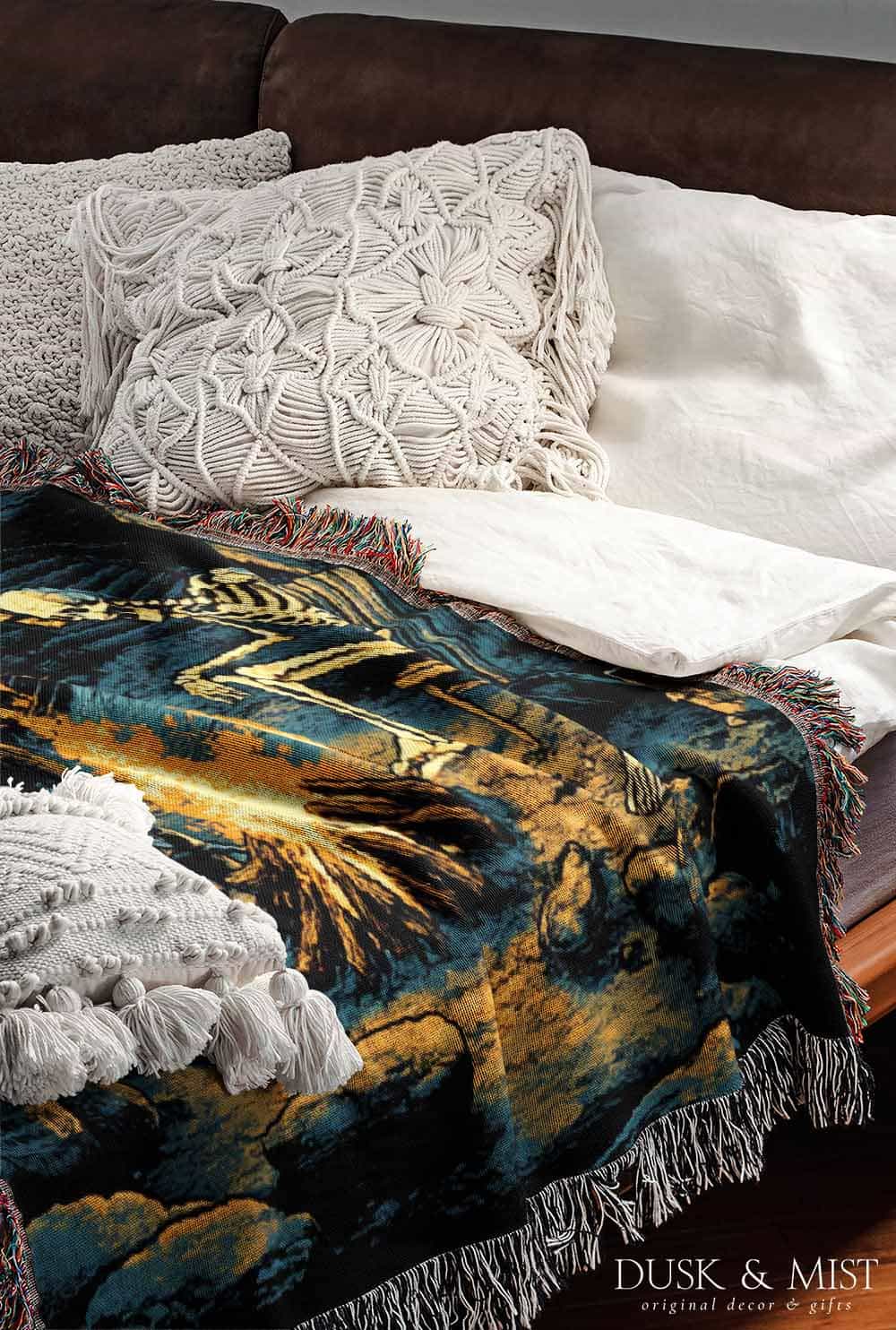 Woven cotton blanket showing two skeletons sitting around a campfire with a bear, log cabin, and full moon in a forest night scene.