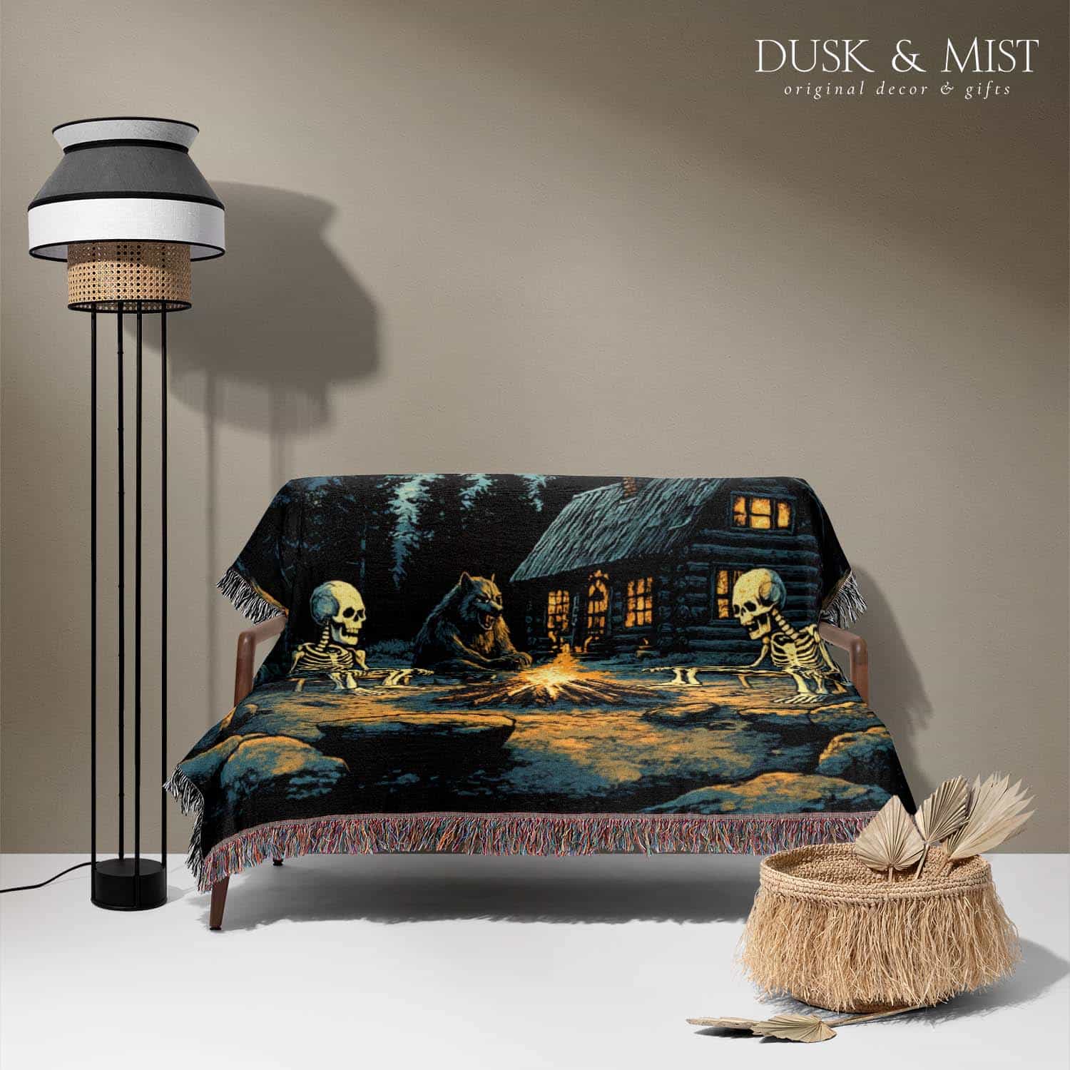 Woven cotton blanket showing two skeletons sitting around a campfire with a bear, log cabin, and full moon in a forest night scene.