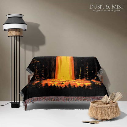 Woven cotton blanket featuring a UFO with a fiery orange beam illuminating a dark forest, with glowing clouds and night sky details.