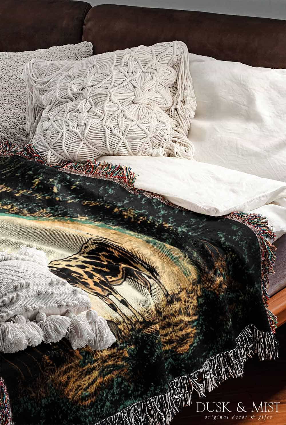 Woven cotton blanket showing a UFO shining a beam of light onto a cow in a forest clearing under a starry night sky.