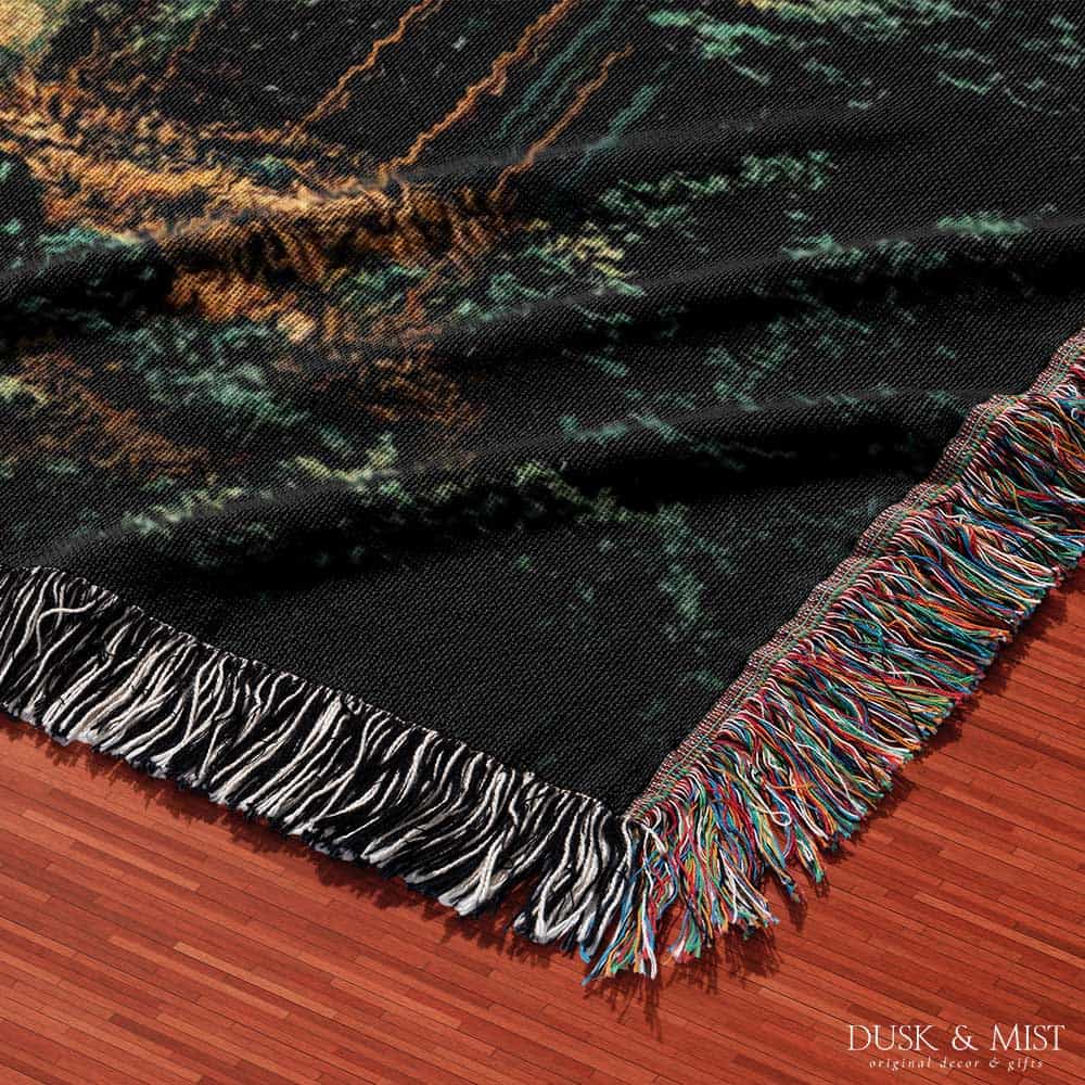 Woven cotton blanket showing a UFO shining a beam of light onto a cow in a forest clearing under a starry night sky.