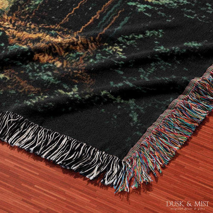 Woven cotton blanket showing a UFO shining a beam of light onto a cow in a forest clearing under a starry night sky.