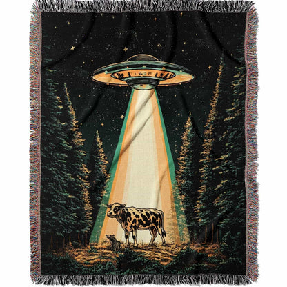 Woven cotton blanket showing a UFO shining a beam of light onto a cow in a forest clearing under a starry night sky.