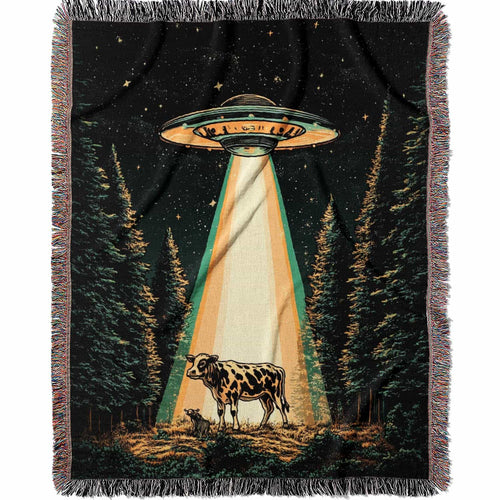 Woven cotton blanket showing a UFO shining a beam of light onto a cow in a forest clearing under a starry night sky.