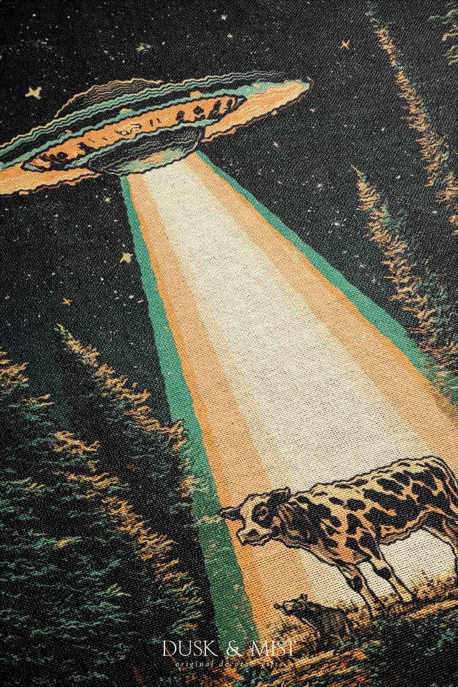 Woven cotton blanket showing a UFO shining a beam of light onto a cow in a forest clearing under a starry night sky.