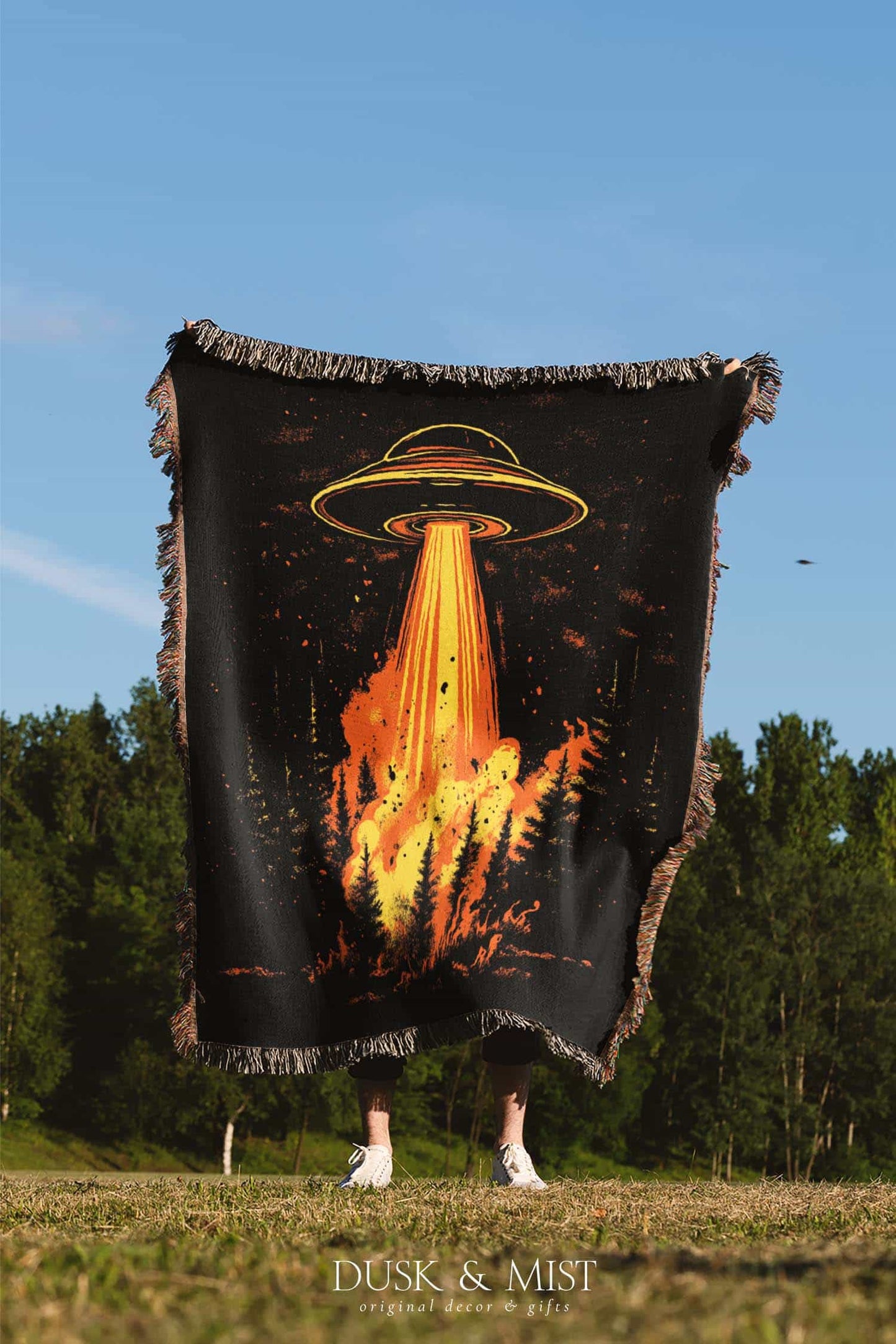 Woven cotton blanket featuring a UFO with a fiery orange beam blasting into a dark forest, with glowing explosions and cosmic night details.