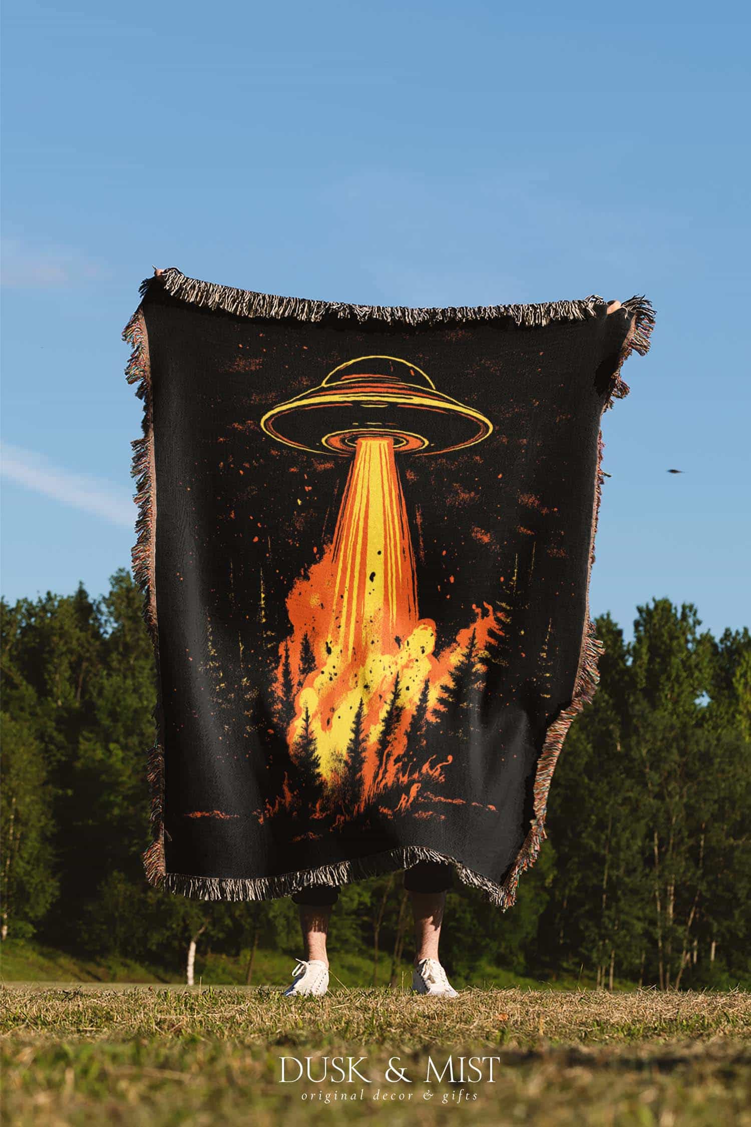 Woven cotton blanket featuring a UFO with a fiery orange beam blasting into a dark forest, with glowing explosions and cosmic night details.