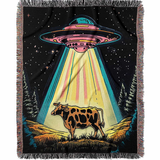 Blanket with a UFO abduction of a cow design against a starry night sky.