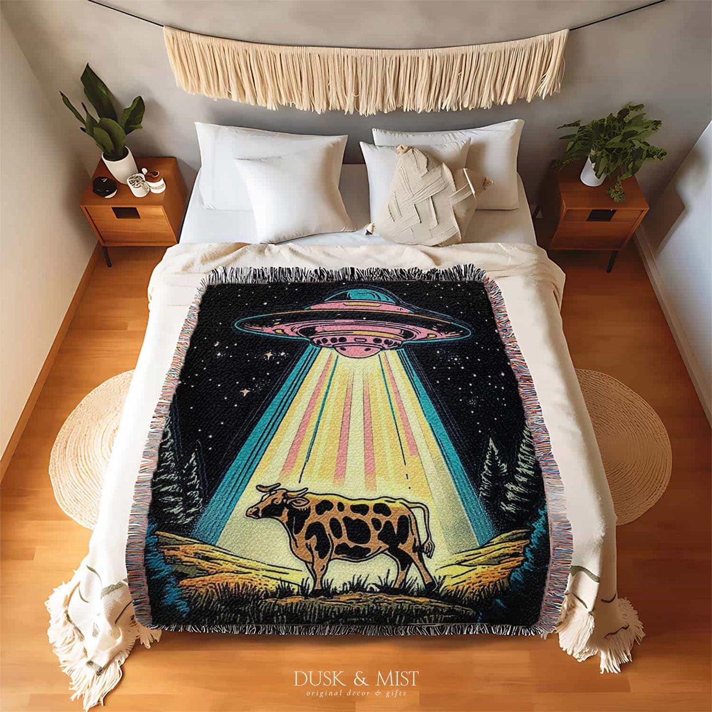 Blanket with a UFO abduction of a cow design against a starry night sky.