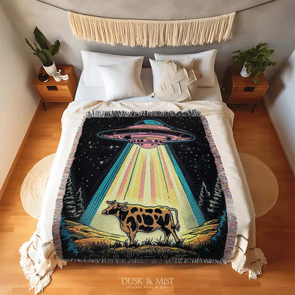 Blanket with a UFO abduction of a cow design against a starry night sky.