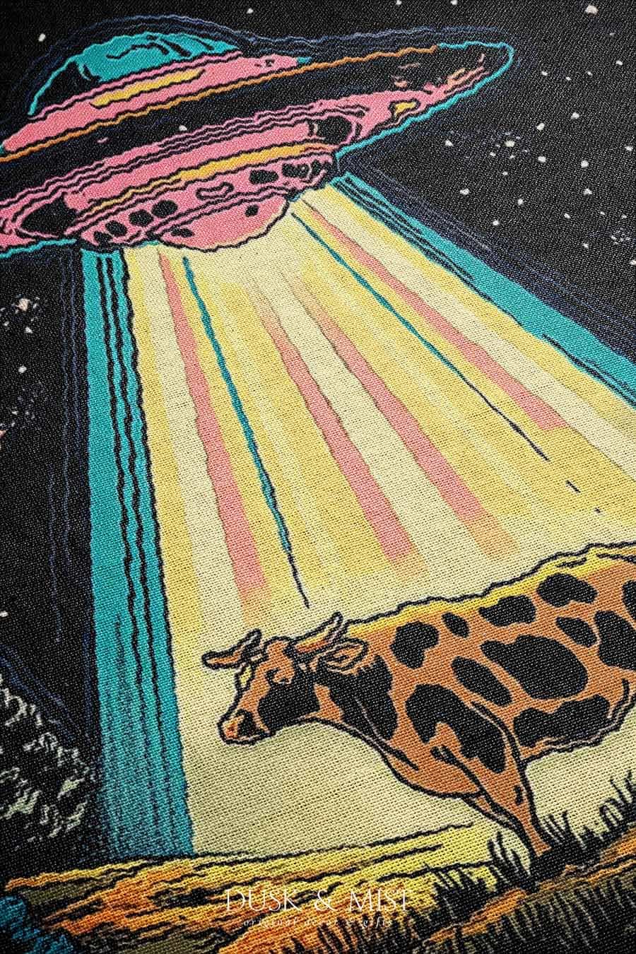 Blanket with a UFO abduction of a cow design against a starry night sky.